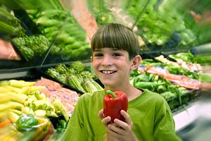 Junge hält Paprika vor Gemüseregal