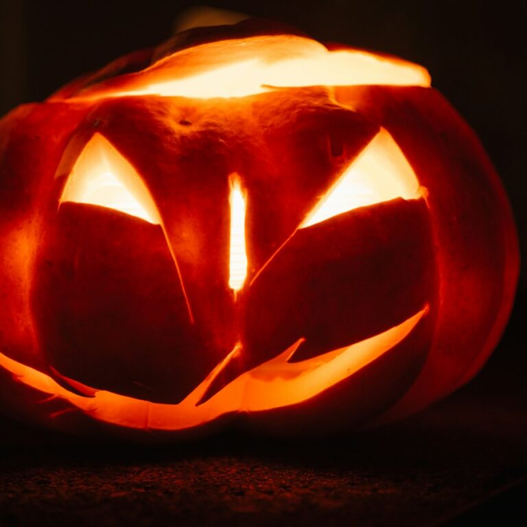 Von innen beleuchteter Halloween-Kürbis mit geschnitztem Gesicht in der Dunkelheit