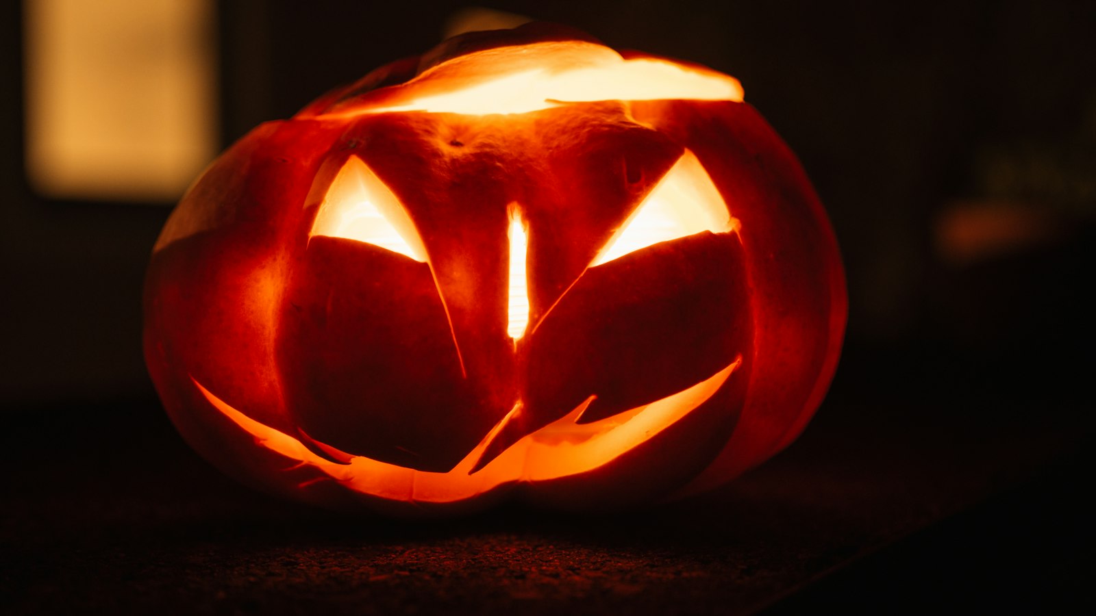Von innen beleuchteter Halloween-Kürbis mit geschnitztem Gesicht in der Dunkelheit